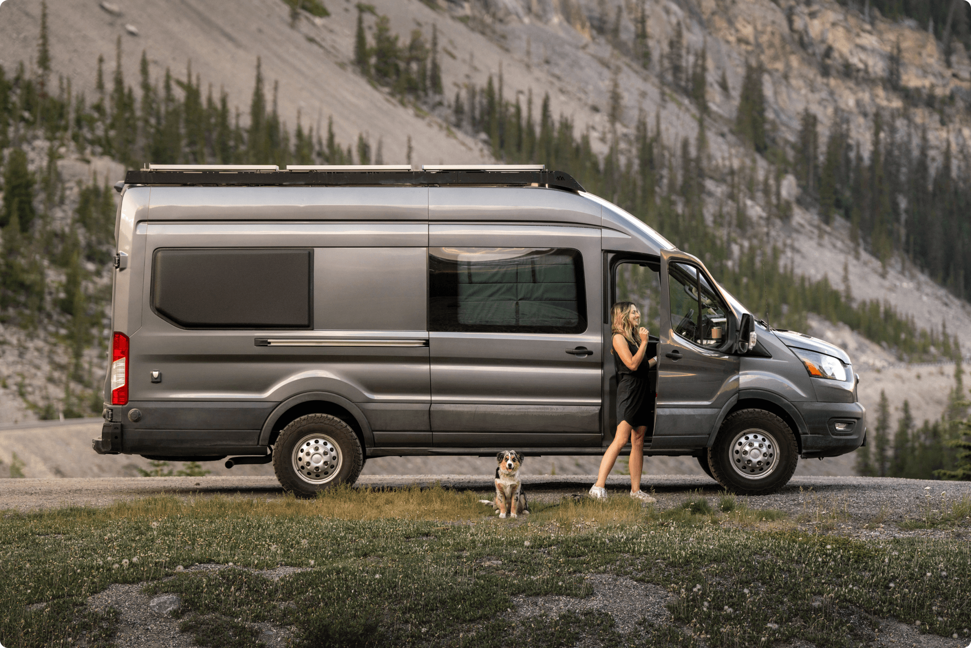Woman and dog next to a campervan at the foot of a mountain